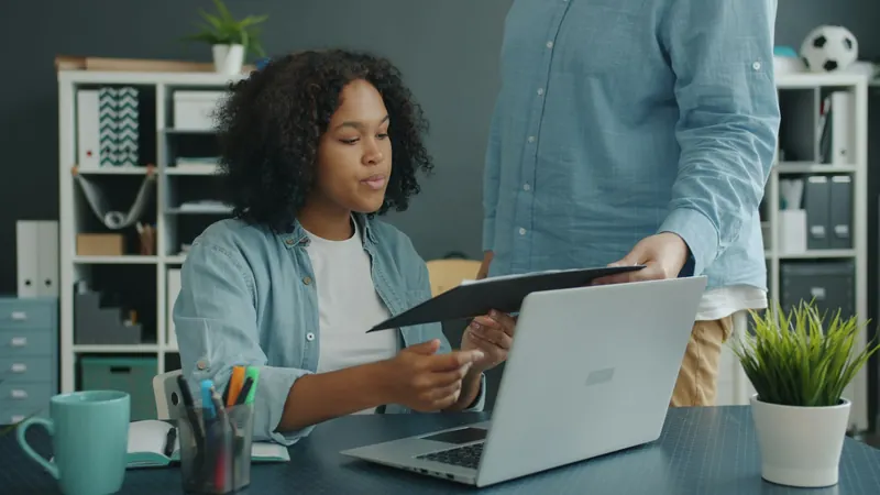 Two people reviewing a document beside a laptop.